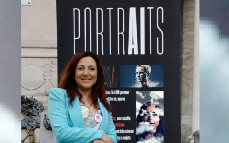 Smiling woman in a turquoise blazer standing in front of a large poster that reads PORTRAITS in white letters.