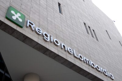 Facade of Regione Lombardia government building with a green emblem sign and silver lettering on a beige tiled wall.
