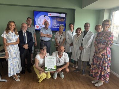 Group of medical staff and guests posing for a photo in a clinic, with a presentation screen in the background.
