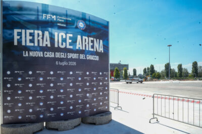 Large blue sign reading 'FIERA ICE ARENA' with subtitle and date, set up outdoors.